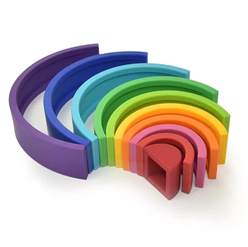 Arco-íris de encaixe feito de tiras de silicone nas cores vinho, vermelho, rosa, laranja, amarelo, verde limão, verde, azul claro, azul escuro, roxo. Peças desmontáveis para brincar e empilhar e encaixar. Peças colocadas em outro formato para ilustrar ourtos modos de brincar.