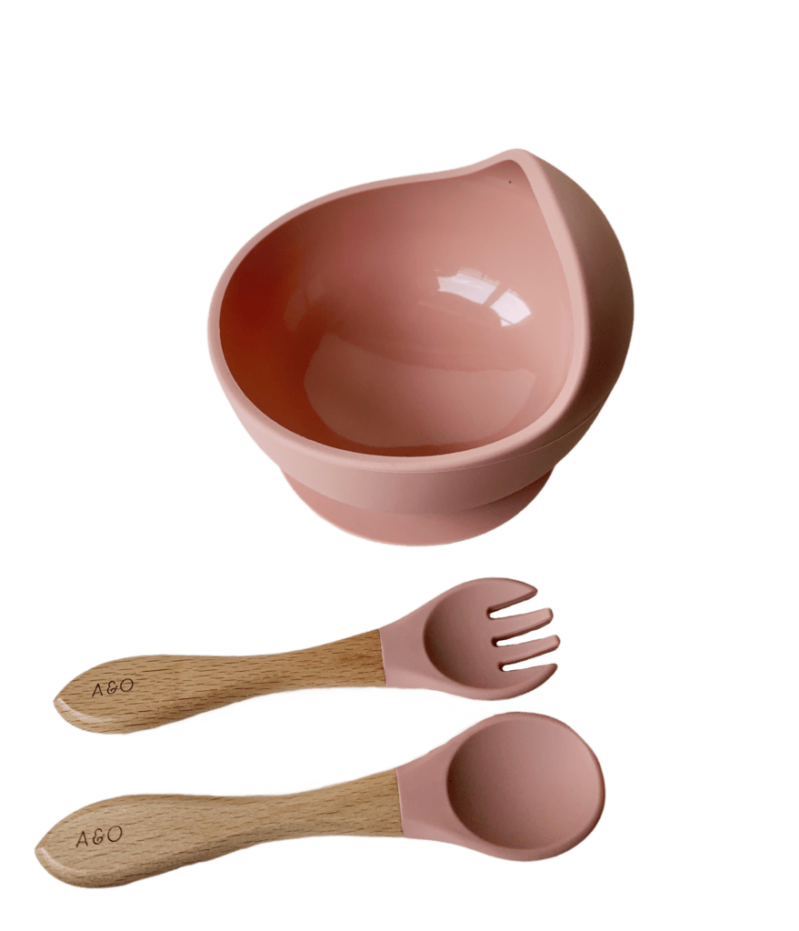 Um bowl com uma colher e um garfo com cabo de madeira e ponteira de silicone na cor rosa blush