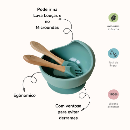 Um bowl com uma colher e um garfo com cabo de madeira e ponteira de silicone na cor verde sage. A imagem contem informações sobre o o produto.